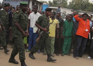 Soldier walks in handcuffs with crowd looking on