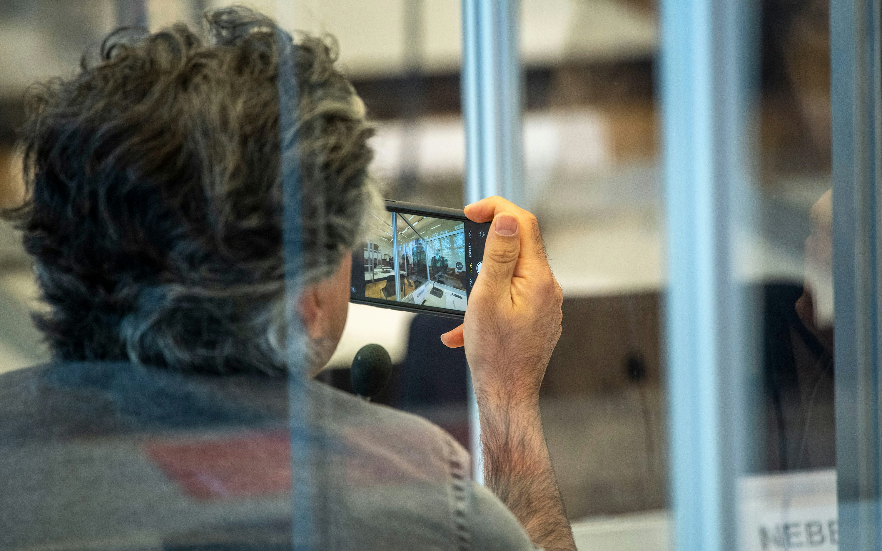 A man photographed through plexiglass panels taking a photo with a mobile phone
