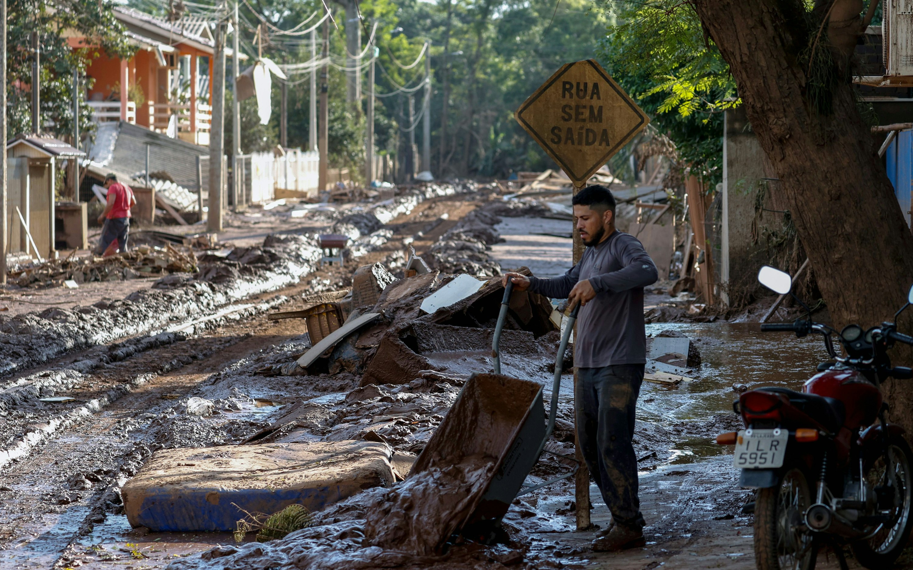 A man tips a wheelbarrow of mud out onto a devastated street in Cruzeiro do Sul, Brazil, on May 8, 2024