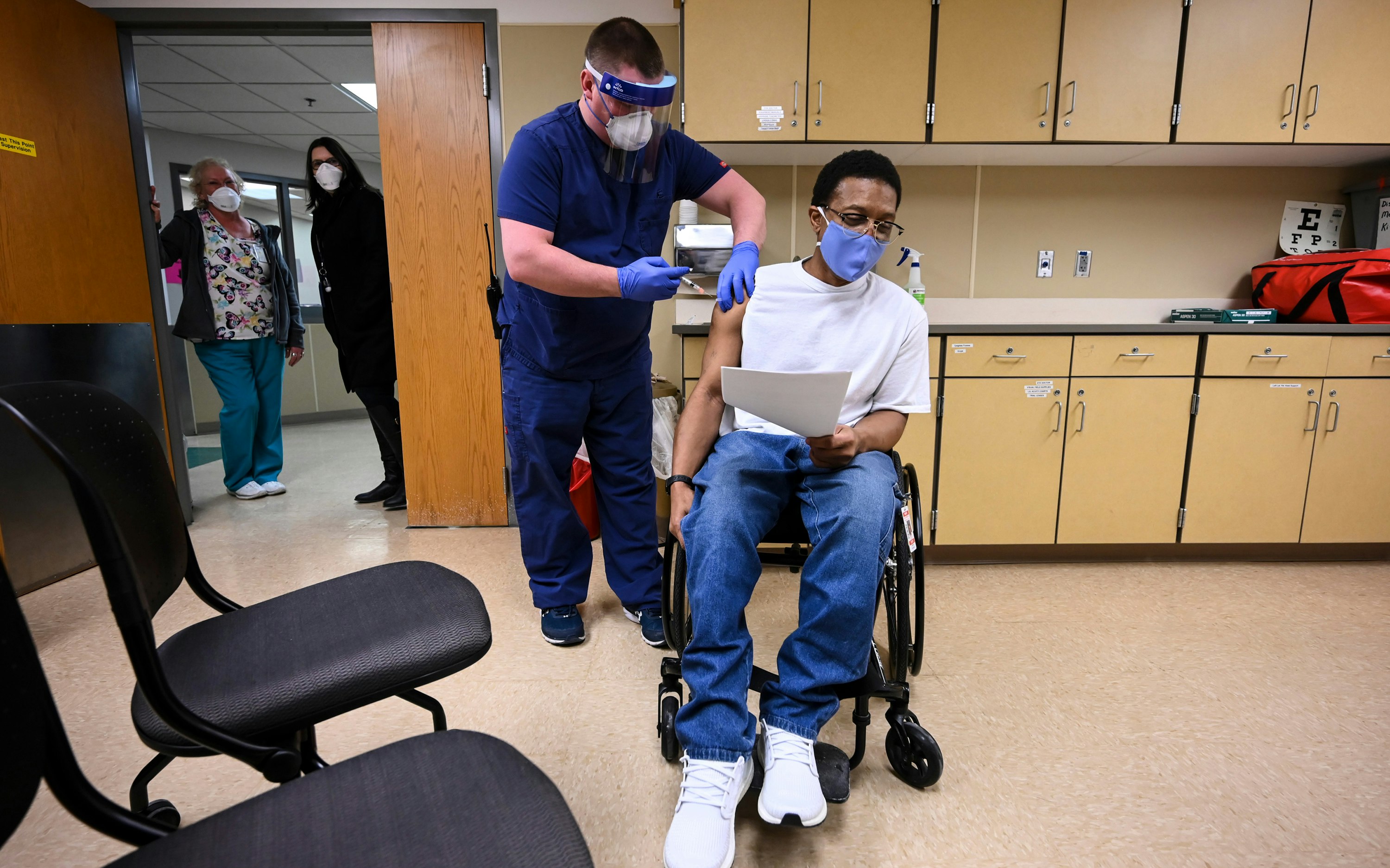 A medical worker injects a person sitting in a wheelchair with a needle