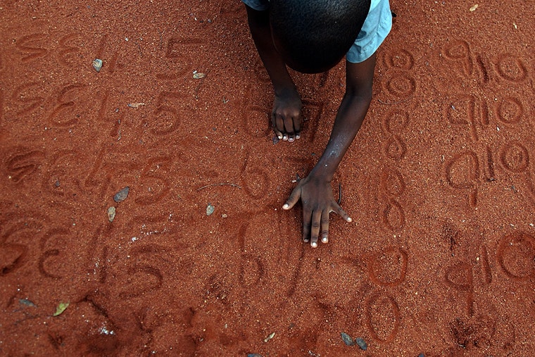 A boy writing numbers in the sand
