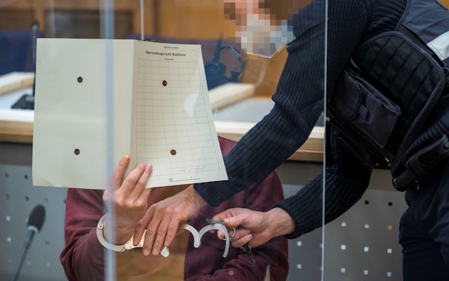 A man in handcuffs hides his face in a courtroom