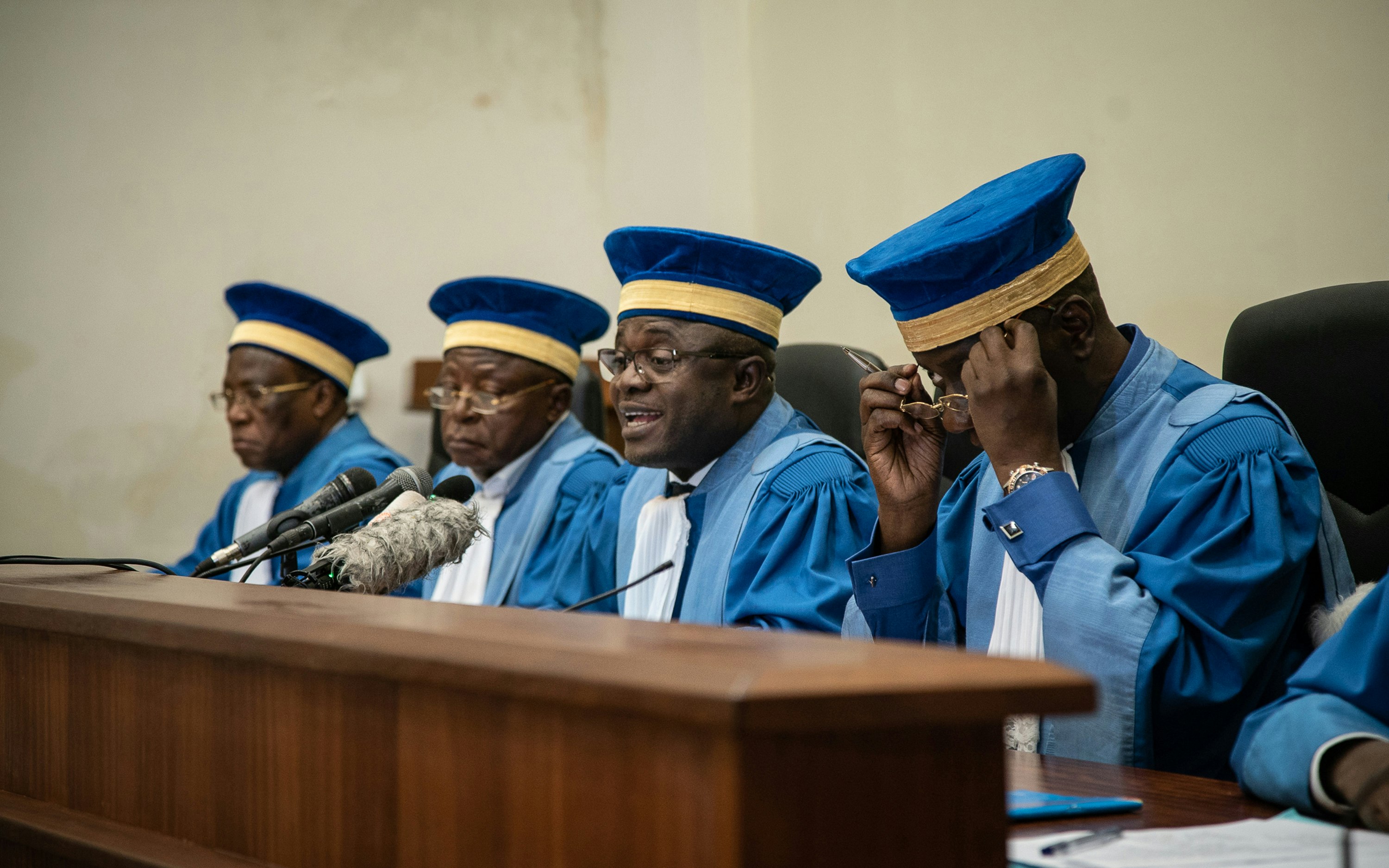 Judges wearing blue caps and robes sit atop a bench in a courtroom